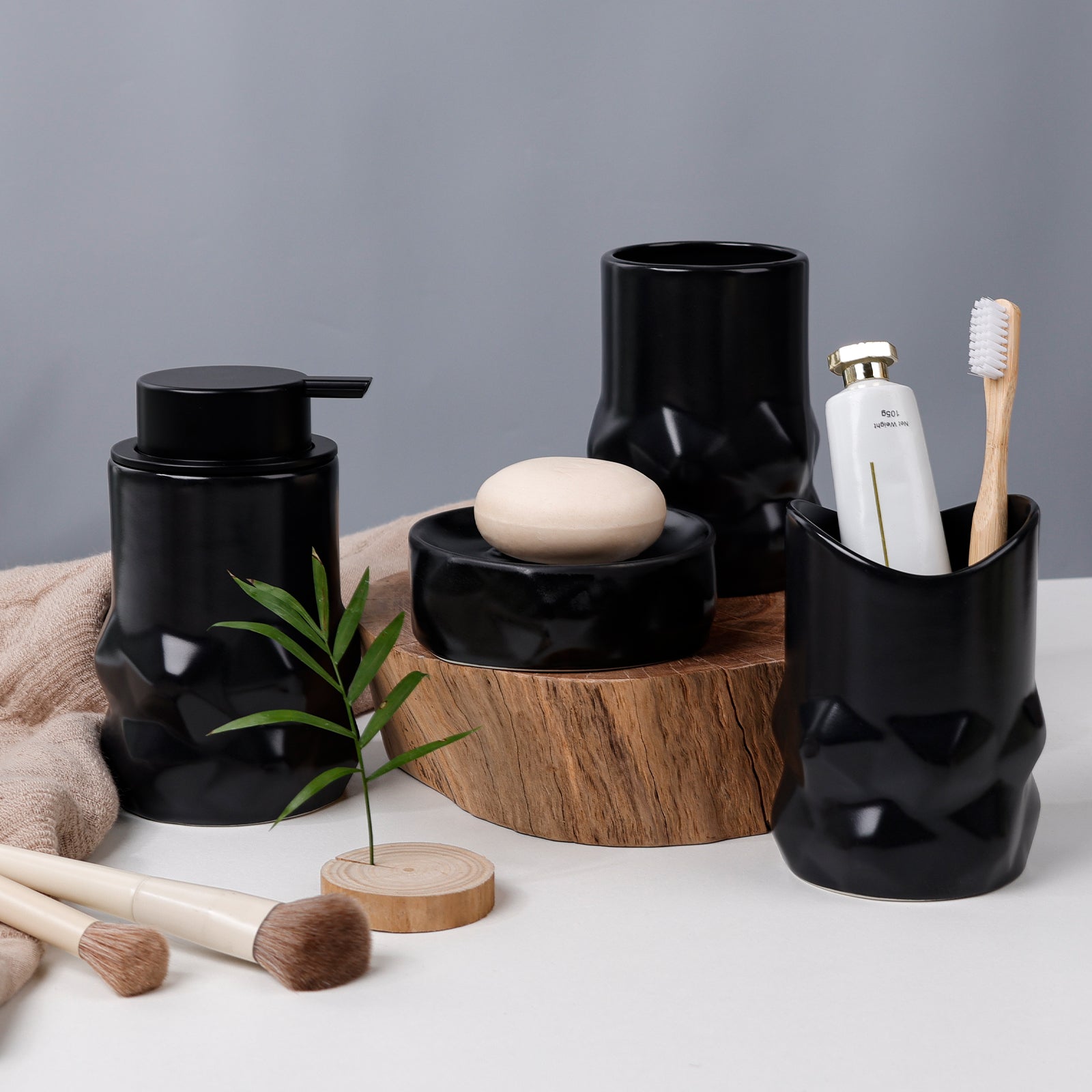 Black ceramic bathroom accessories including a soap dish, toothbrush holder, and dispenser on a white surface with a gray background.