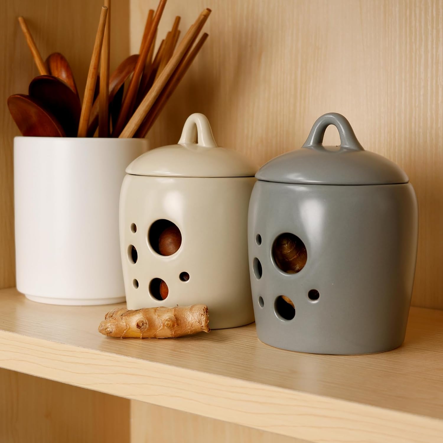 Two ceramic jars with wooden utensils and ginger root on a wooden shelf.