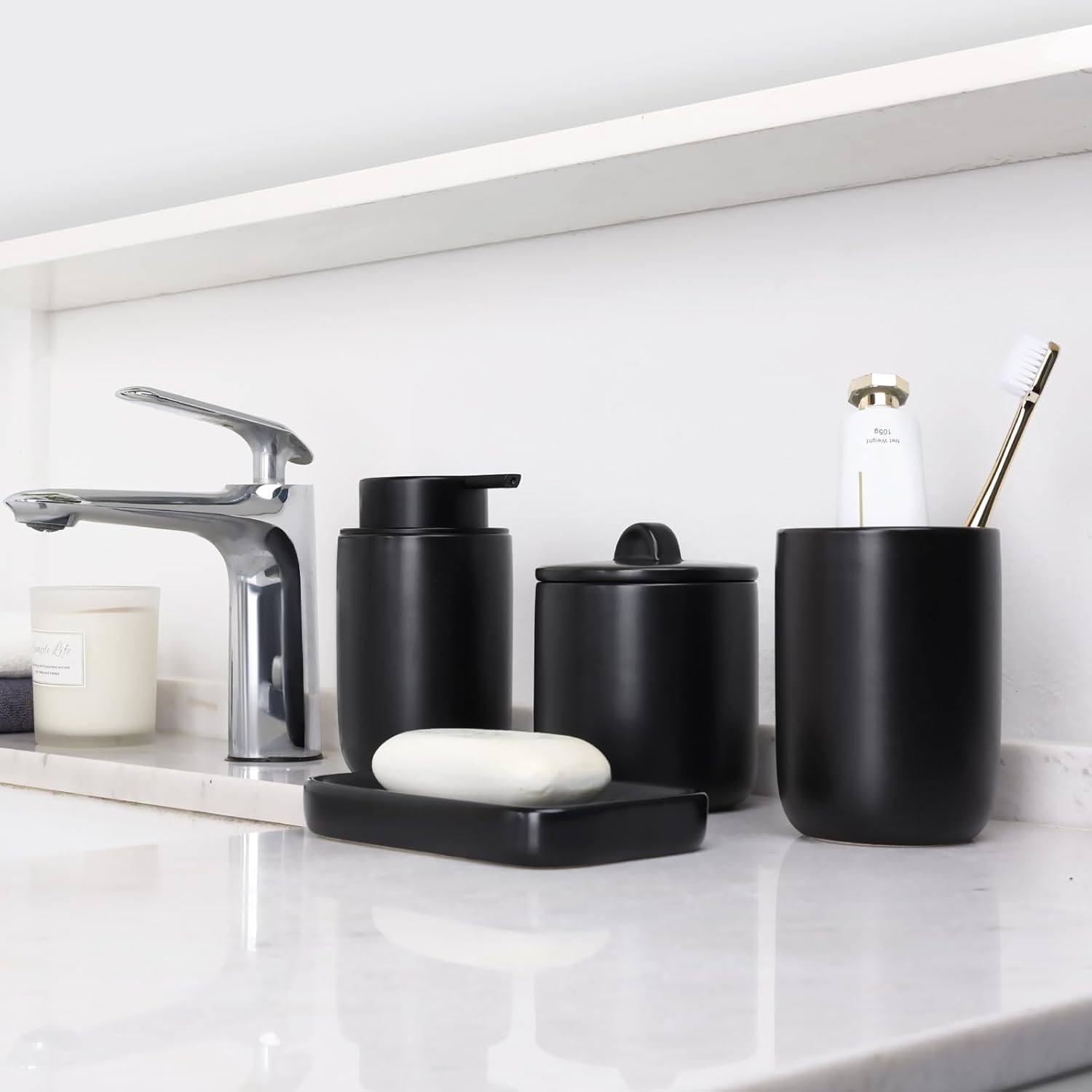 Lifestyle shot of the BosilunLife 4-piece foaming bathroom accessory set in minimalist matte black recycled eco-clay. Styled on a white marble washbasin alongside a sleek chrome tap and a glass candle, the collection includes a manual soap dispenser, a rectangular soap dish holding white soap, a lidded apothecary jar, and a toothbrush holder, creating a striking, high-contrast modern aesthetic.