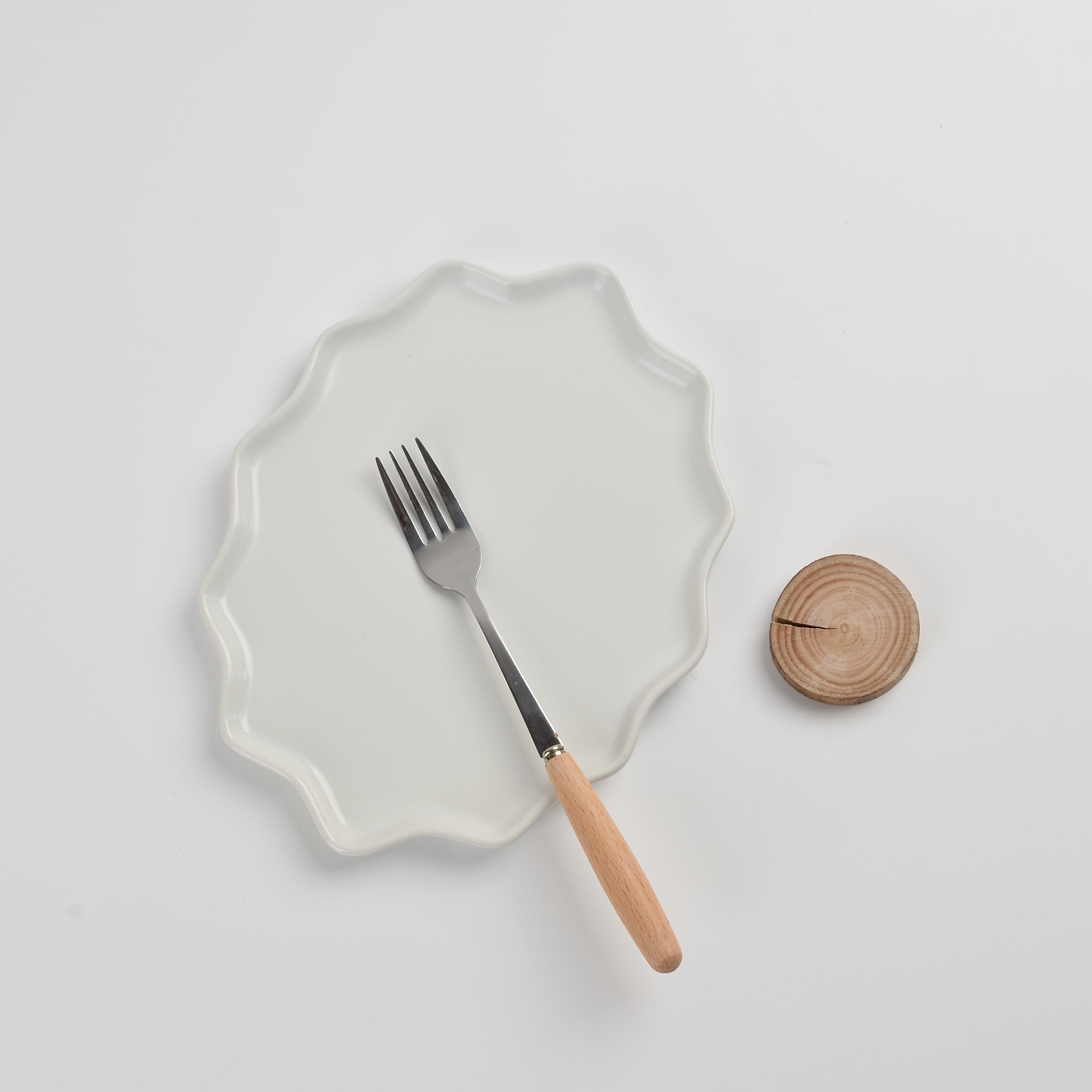 White plate with a fork and wooden coaster on a light gray background