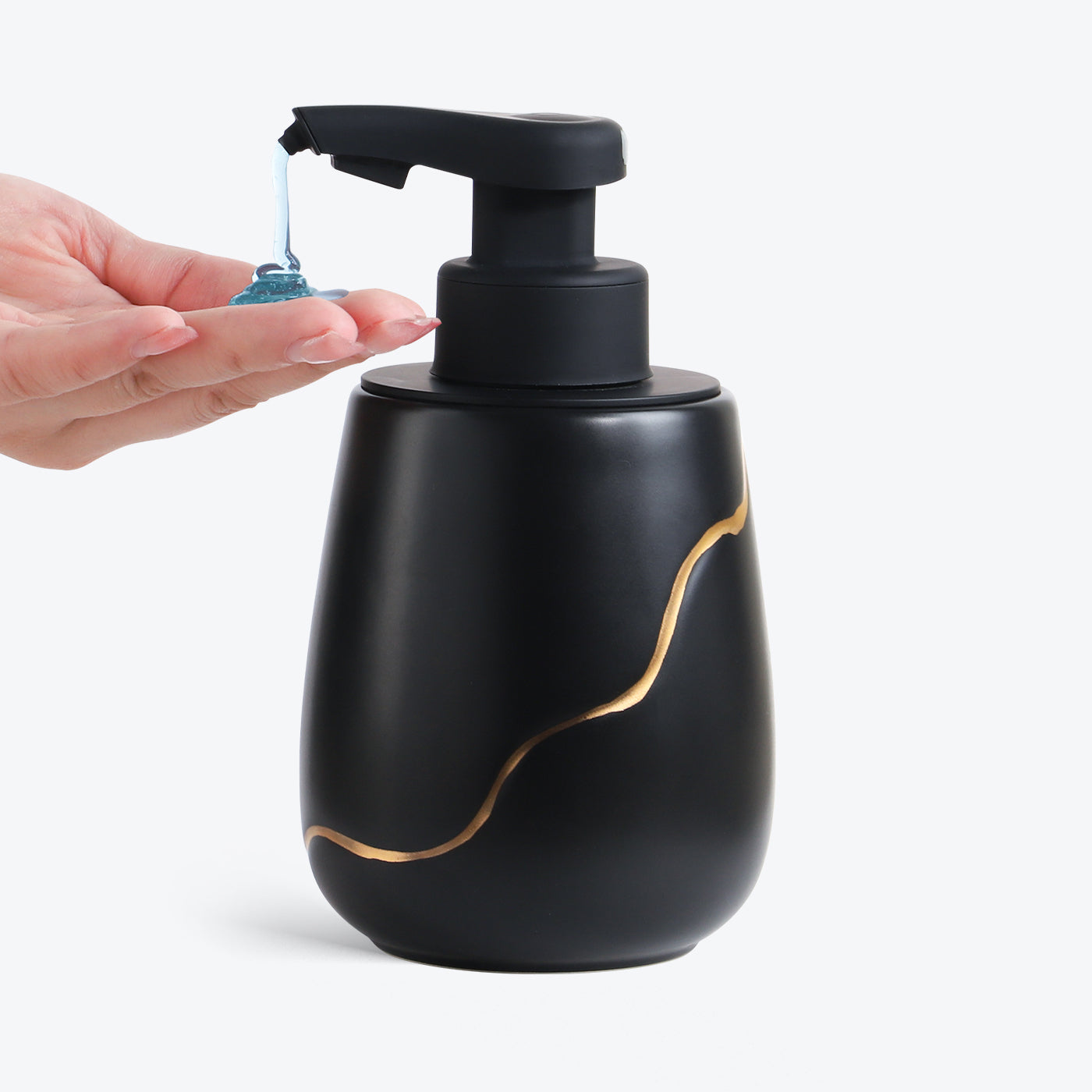 Black soap dispenser with gold accents being used by a hand on a white background