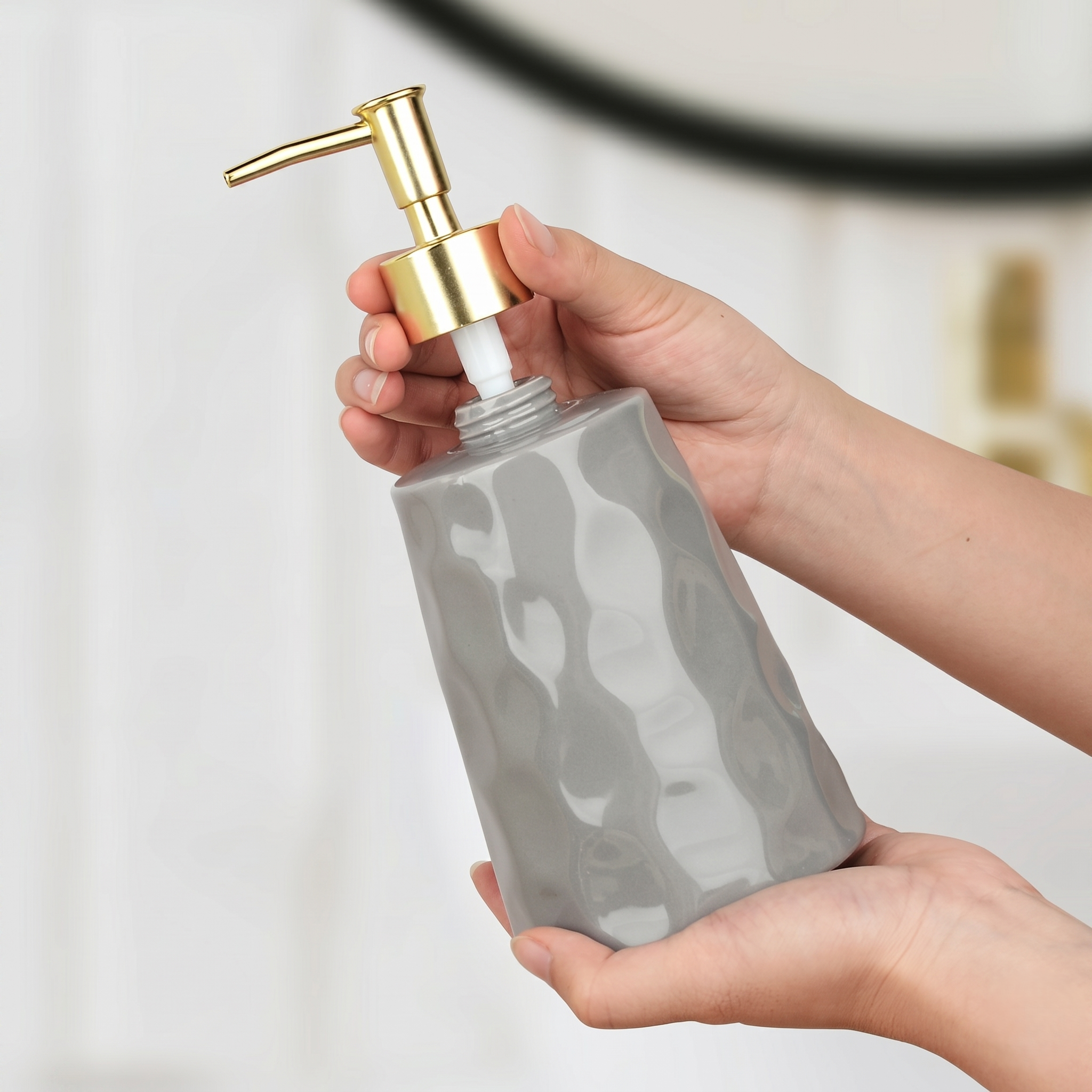 Close-up of a person's hands unscrewing the gold pump from the BosilunLife Bring Nature Inside grey liquid soap dispenser. The image demonstrates the easy-to-refill design of the glossy, rippled recycled eco-clay bottle, highlighting sustainable and practical bathroom utility.