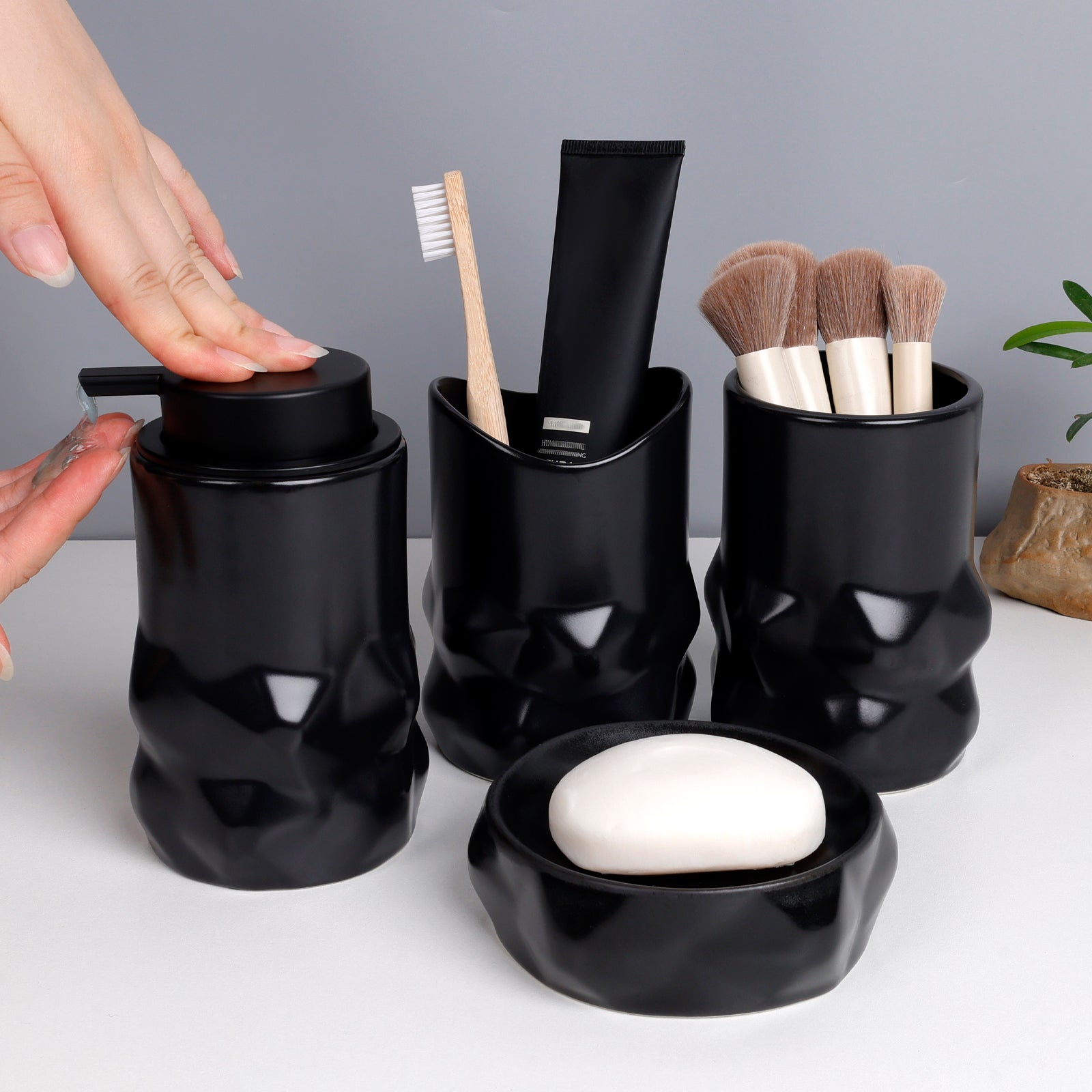 Black bathroom accessories set with a hand reaching for a soap dispenser.