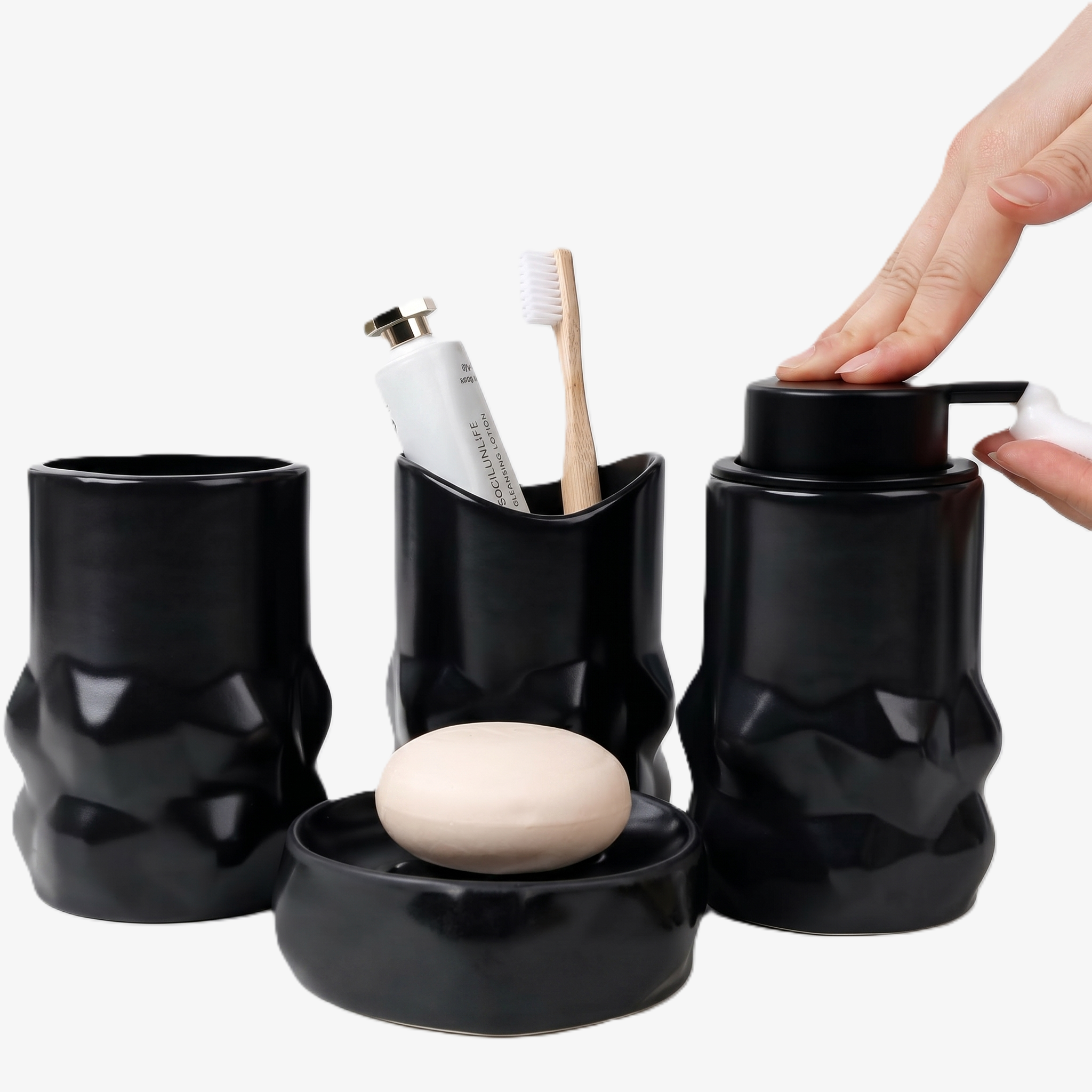 BosilunLife 4-piece diamond-shaped foaming bathroom accessory set in matte black recycled eco-clay. The sculptural, faceted collection features a person's hand pressing down on the manual soap dispenser to release rich white foam. Alongside it sits a textured tumbler, a toothbrush holder containing a bamboo toothbrush, and a round soap dish holding a bar of soap, creating a striking, modern washroom aesthetic.