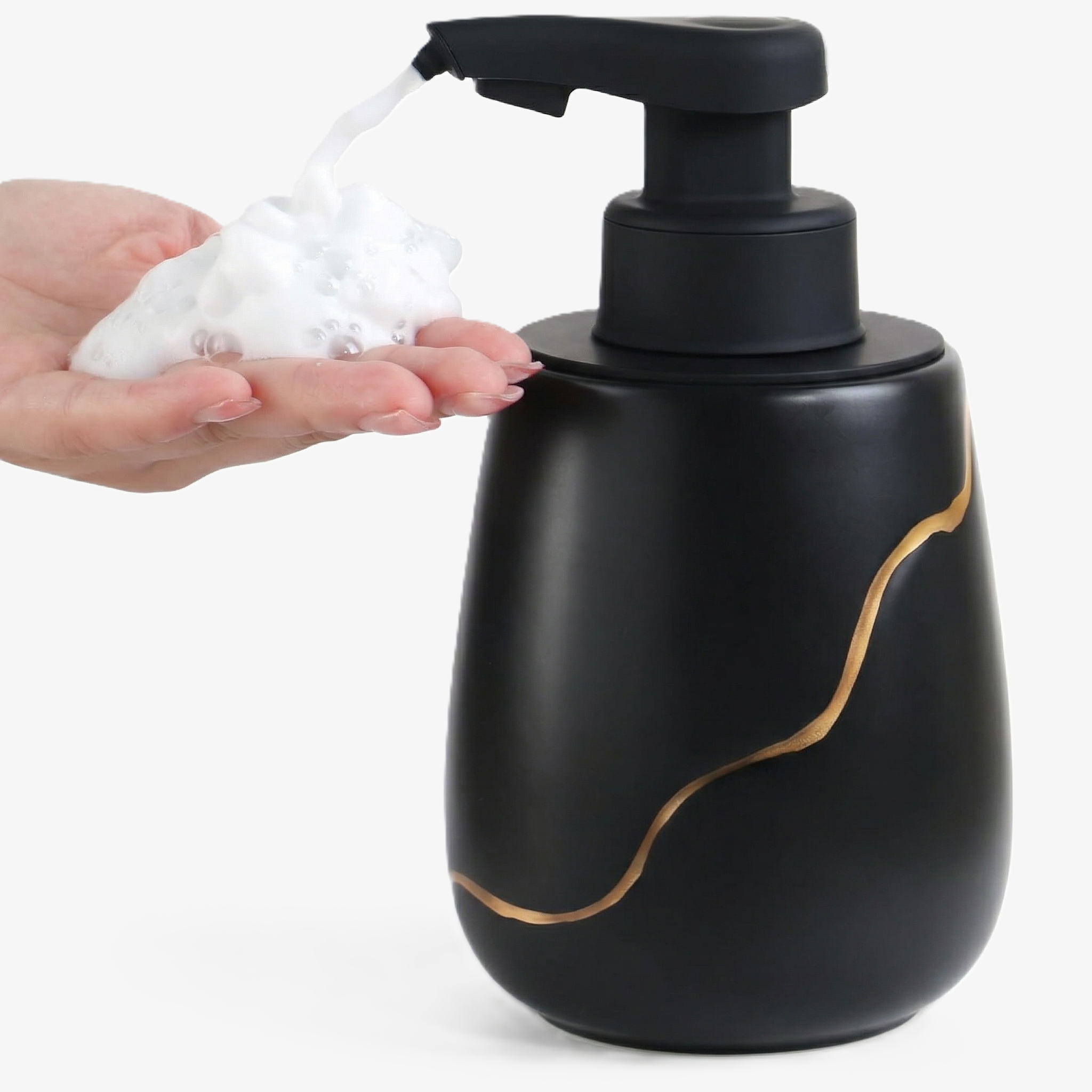 A hand receiving foam from the 17 oz BosilunLife automatic touchless soap dispenser, featuring a matte black recycled eco-clay body with an elegant gold wave design.